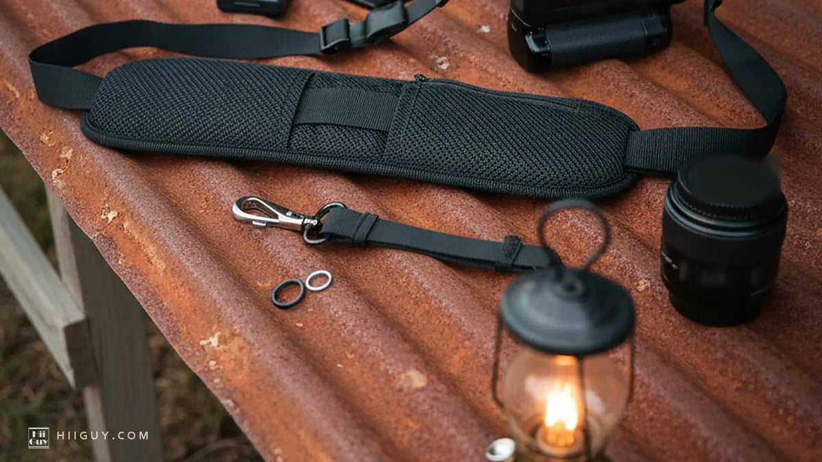 Wide padded camera strap lying open on rusted iron, its narrow webbing running out both ends, lantern lit nearby
