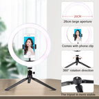 LED ring light on a small black tripod holding a phone on a makeup table, with a woman applying blusher behind it