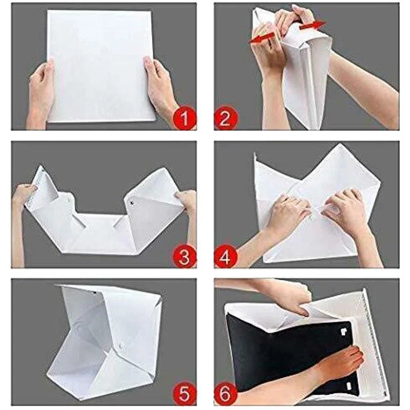 Hands holding a DSLR in front of a lit white folding light box with gold beaded bracelets on its floor