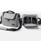 Grey camera shoulder bag with a black top handle and strap, beside an open one holding a DSLR and a lens
