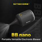 Hand holding a small black Nitecore BB Nano electric blower with a tapered rubber nozzle