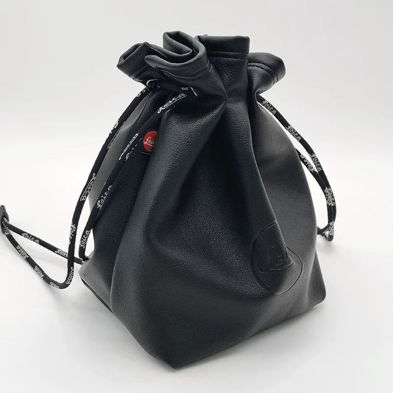 Black leather drawstring pouch opened around a compact camera with a round lens cap, on a store counter