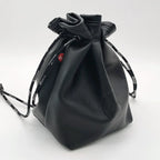 Black leather drawstring pouch opened around a compact camera with a round lens cap, on a store counter