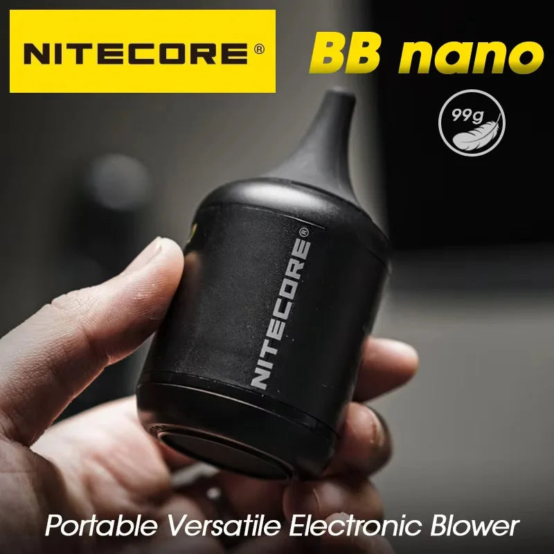 Hand holding a small black Nitecore BB Nano electric blower with a tapered rubber nozzle