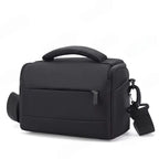 Black camera shoulder bag with a padded top handle, a zip front pocket and a clip-on shoulder strap