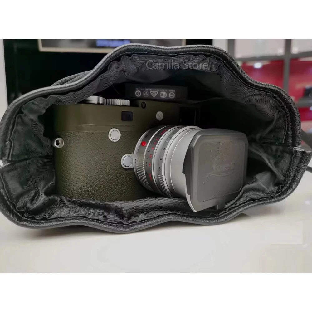Black leather drawstring pouch opened around a compact camera with a round lens cap, on a store counter