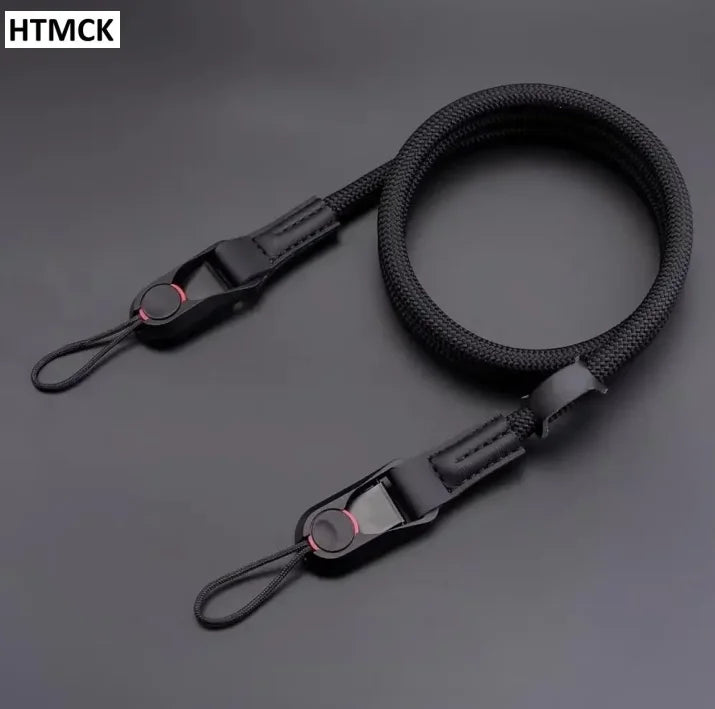 Black braided rope camera strap coiled on a dark surface, with a quick release clip and a cord loop at each end