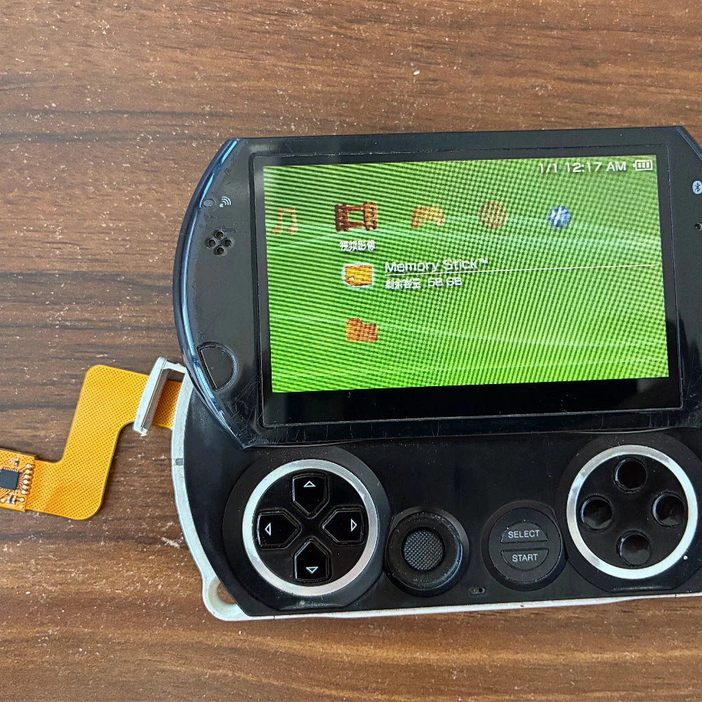 PSP Go console lying face up with an orange ribbon adapter attached at the left edge and a Memory Stick entry on screen
