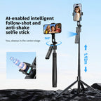 Black selfie stick tripod with a rotating phone mount and a detachable remote, extended tall on rocks with a phone on top