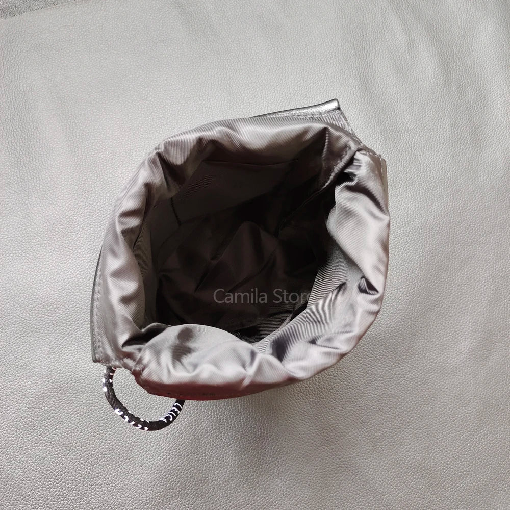 Black leather drawstring pouch opened around a compact camera with a round lens cap, on a store counter