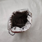 Black leather drawstring pouch opened around a compact camera with a round lens cap, on a store counter