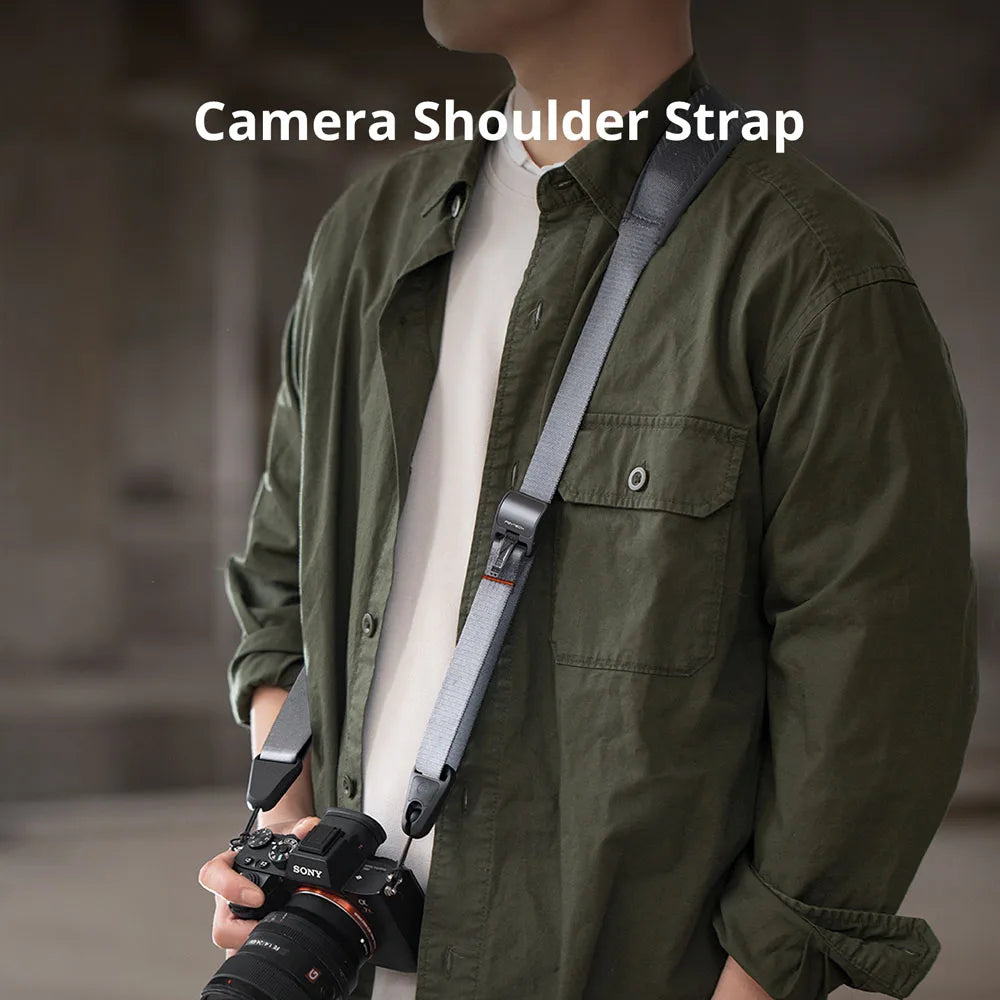Man wearing a light grey camera shoulder strap with a mirrorless camera at his hip, plus the strap in green, black and blue