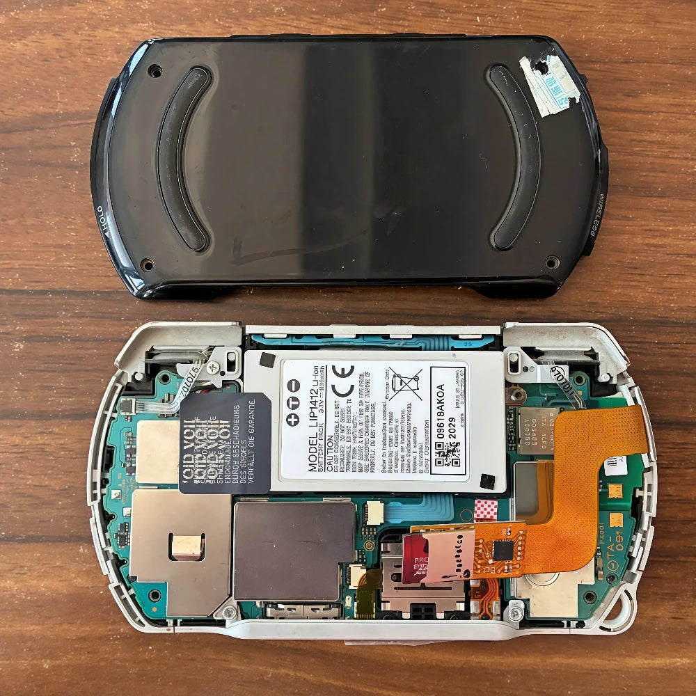 PSP Go console lying face up with an orange ribbon adapter attached at the left edge and a Memory Stick entry on screen