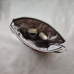 Black leather drawstring pouch opened around a compact camera with a round lens cap, on a store counter