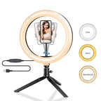LED ring light on a small black tripod holding a phone on a makeup table, with a woman applying blusher behind it