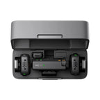Black DJI Mic Mini charging case open, holding two small transmitters with gray furry windscreens