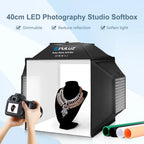 Black Puluz folding light box lit white inside with a necklace on a bust, a camera in hand, four backdrop rolls and EU plug