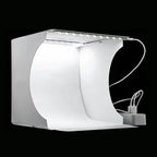 Small white folding light box with a strip of LEDs along the top edge, a cable and a power adapter, on a black background