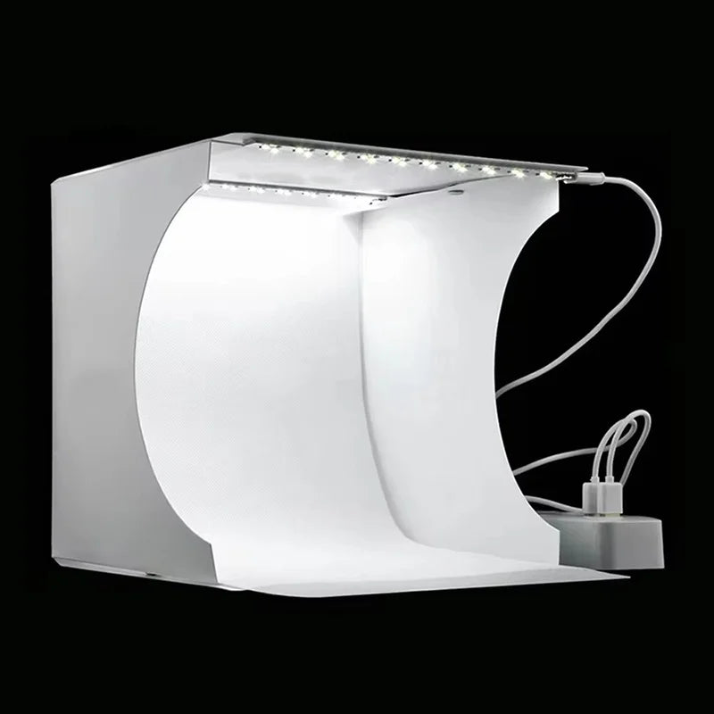 Small white folding light box with a strip of LEDs along the top edge, a cable and a power adapter, on a black background