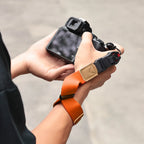 Orange camera wrist strap with a black clip worn on a wrist, the hand holding a black mirrorless camera