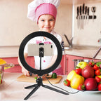 LED ring light on a small black tripod holding a phone on a makeup table, with a woman applying blusher behind it