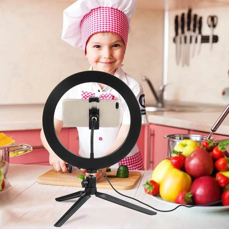 LED ring light on a small black tripod holding a phone on a makeup table, with a woman applying blusher behind it