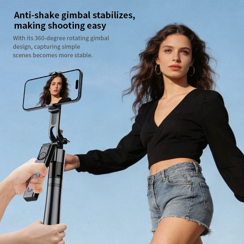Black selfie stick tripod with a rotating phone mount and a detachable remote, extended tall on rocks with a phone on top