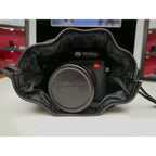 Black leather drawstring pouch opened around a compact camera with a round lens cap, on a store counter