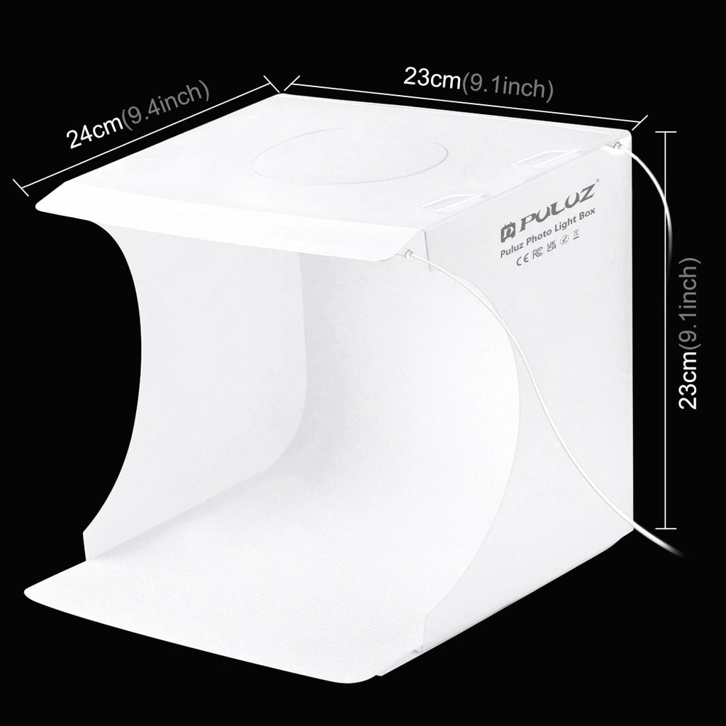 Small white Puluz folding light box lit from above with beaded bracelets inside, and a hand holding a phone showing the shot