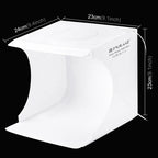 Small white Puluz folding light box lit from above with beaded bracelets inside, and a hand holding a phone showing the shot