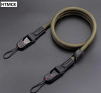 Black braided rope camera strap coiled on a dark surface, with a quick release clip and a cord loop at each end
