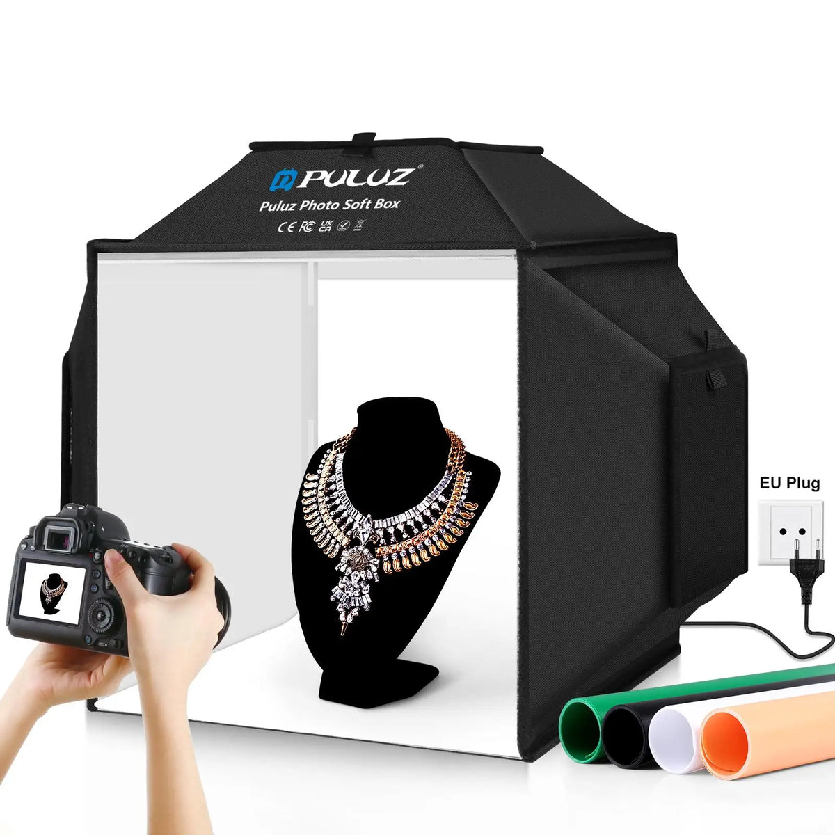 Black Puluz folding light box lit white inside with a necklace on a bust, a camera in hand, four backdrop rolls and EU plug