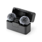 Black DJI Mic Mini charging case open, holding two small transmitters with gray furry windscreens