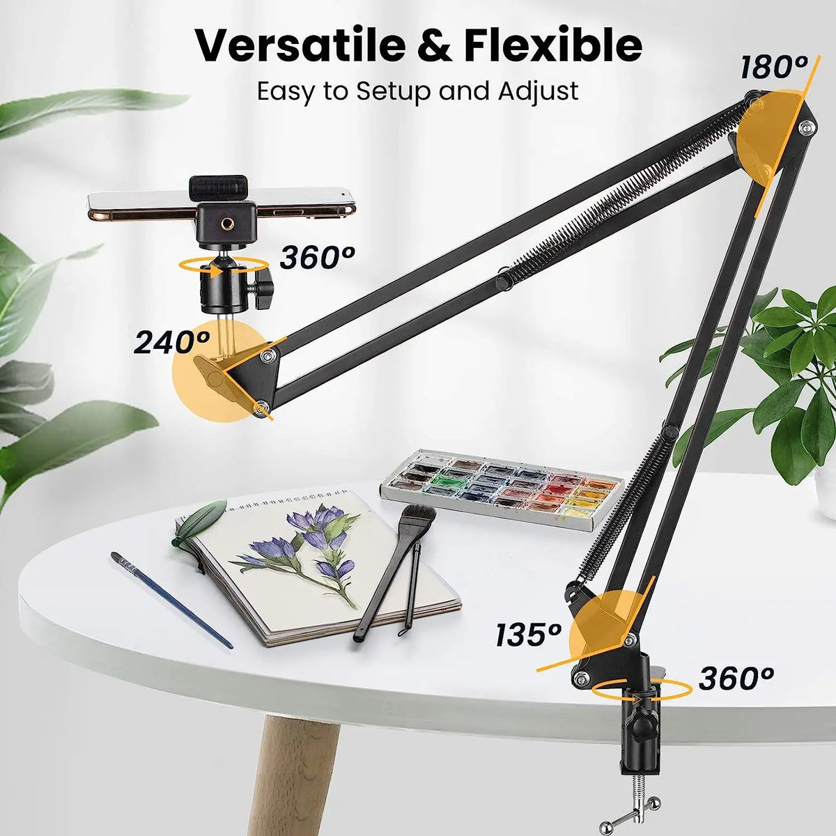 Black spring-loaded desk arm clamped to a table holding a phone, with a remote, ball head, phone clip and clamp laid out
