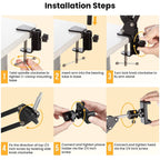 Black spring-loaded desk arm clamped to a table holding a phone, with a remote, ball head, phone clip and clamp laid out