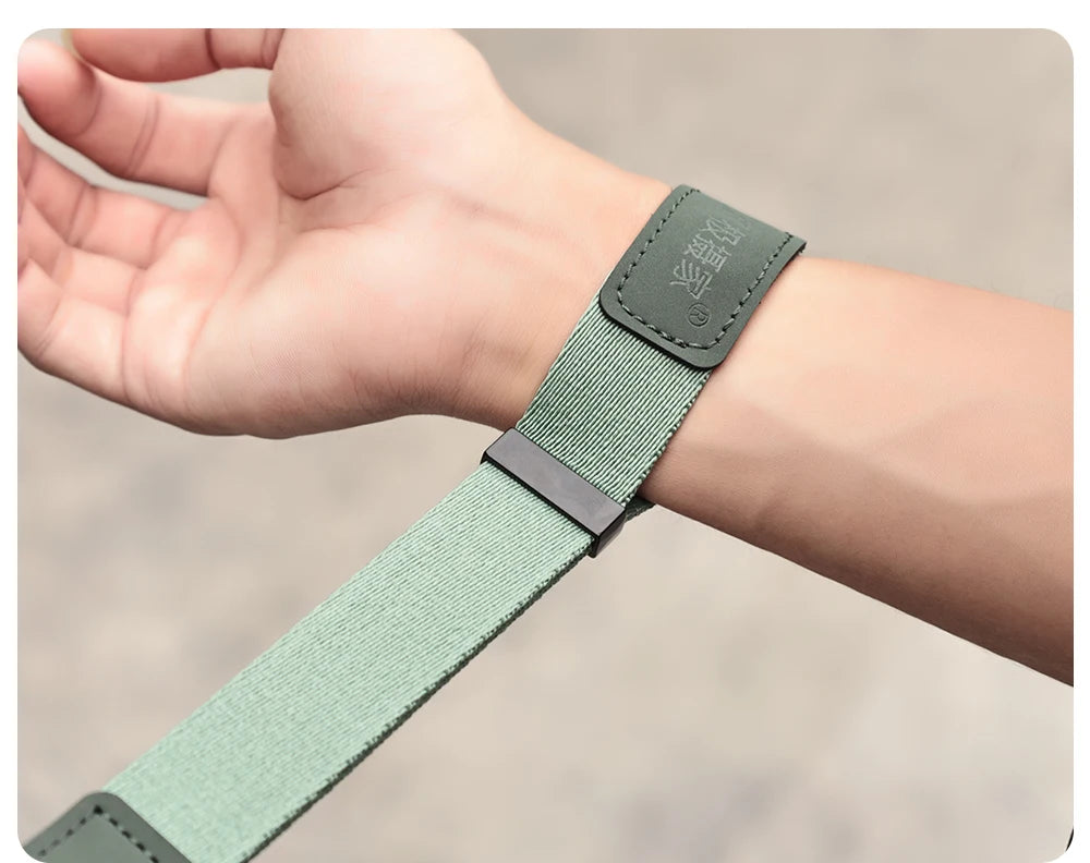 Orange camera wrist strap with a black clip worn on a wrist, the hand holding a black mirrorless camera