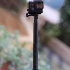 Two black carbon fiber selfie sticks, one long and one short, beside a folding bullet time handle