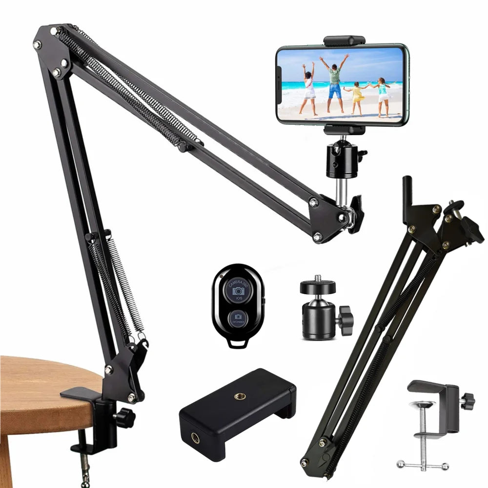 Black spring-loaded desk arm clamped to a table holding a phone, with a remote, ball head, phone clip and clamp laid out